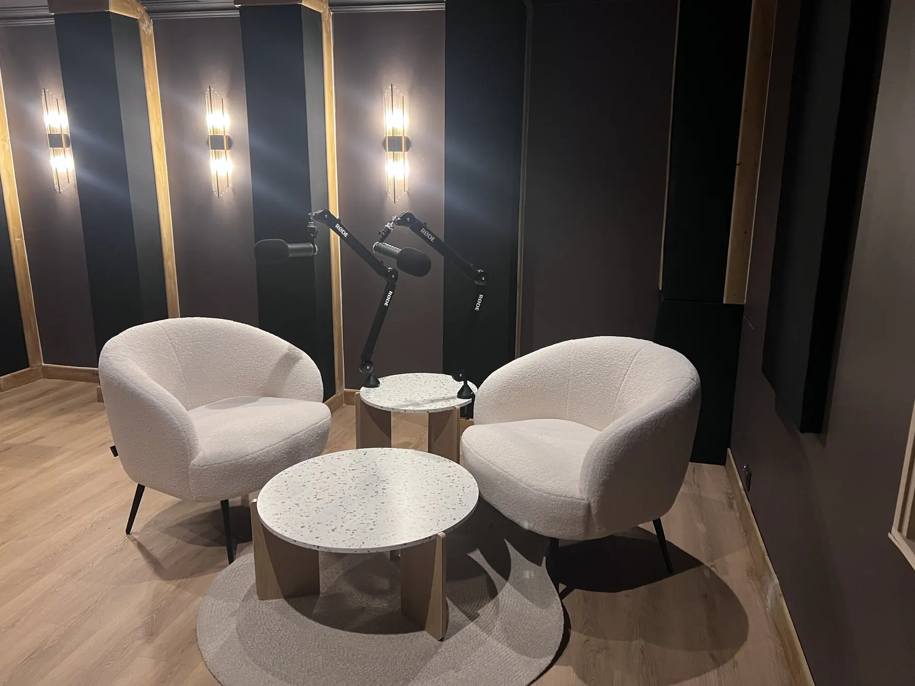 Salle de podcast livrée : panneaux verticaux en cadres bois, appliques intégrées, mobilier clair.